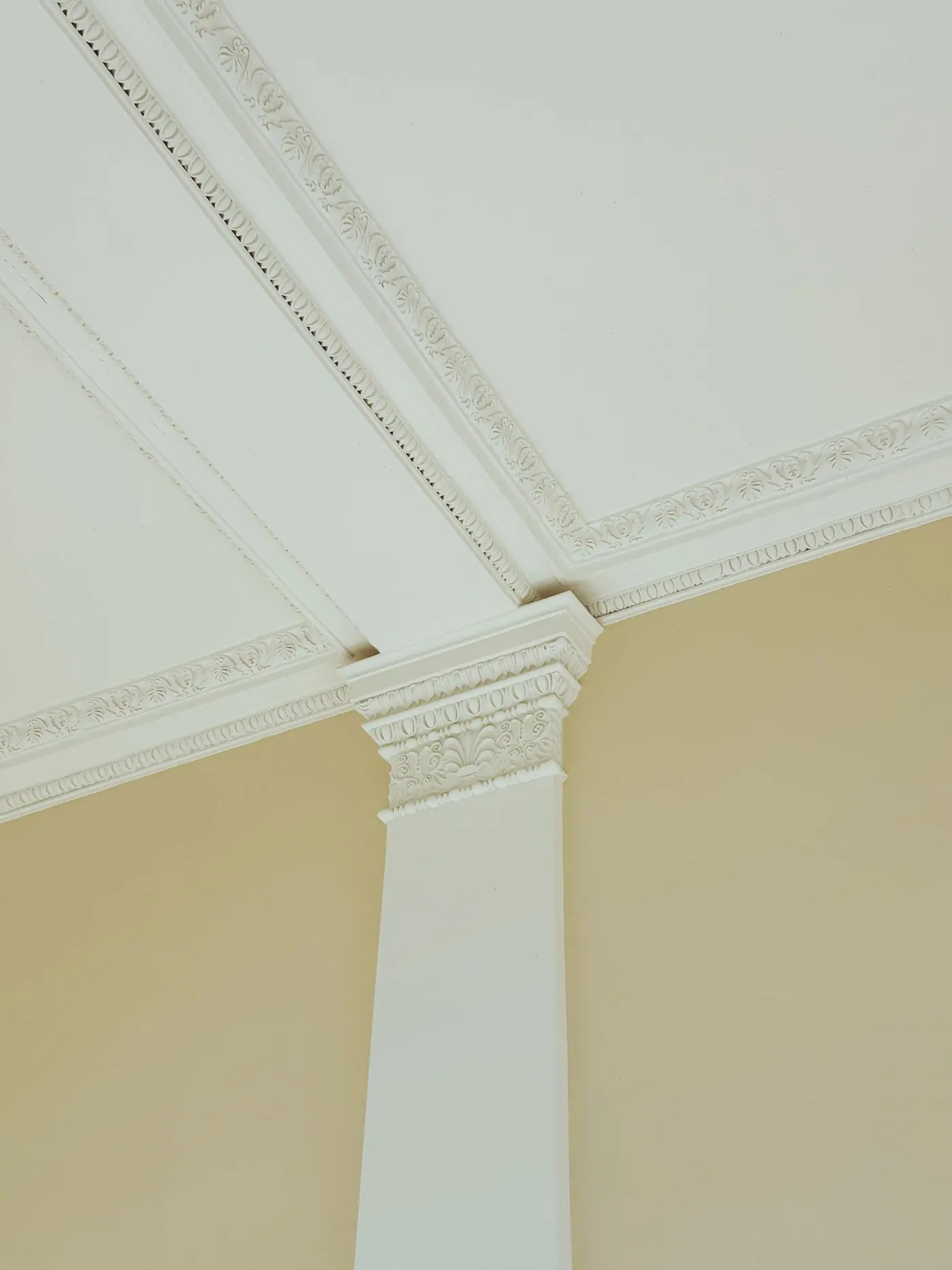 An ornate white plaster cornice running into a fluted column capital in a cream-painted interior
