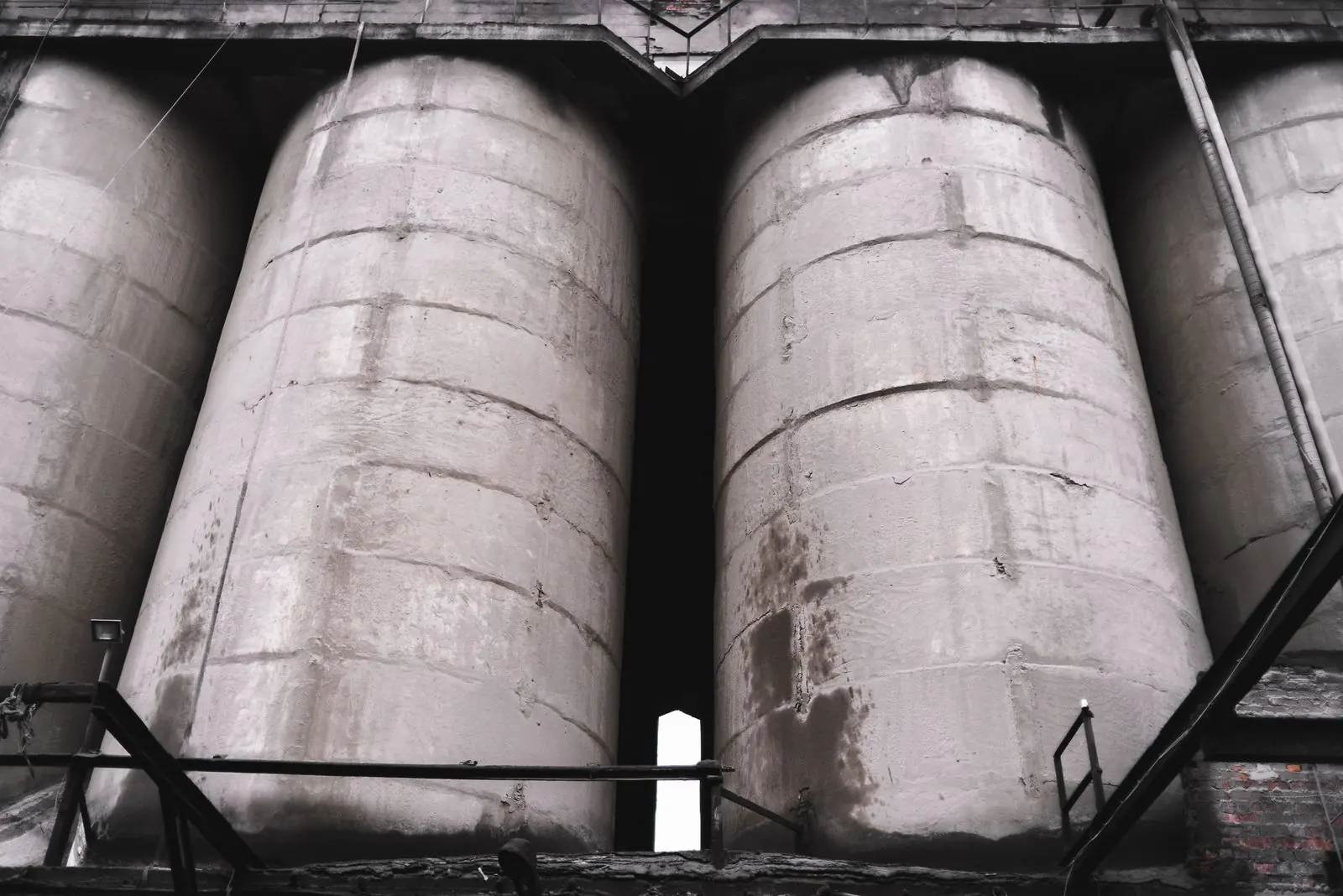 Tall concrete storage silos at an industrial plant, seen from below against an overcast sky