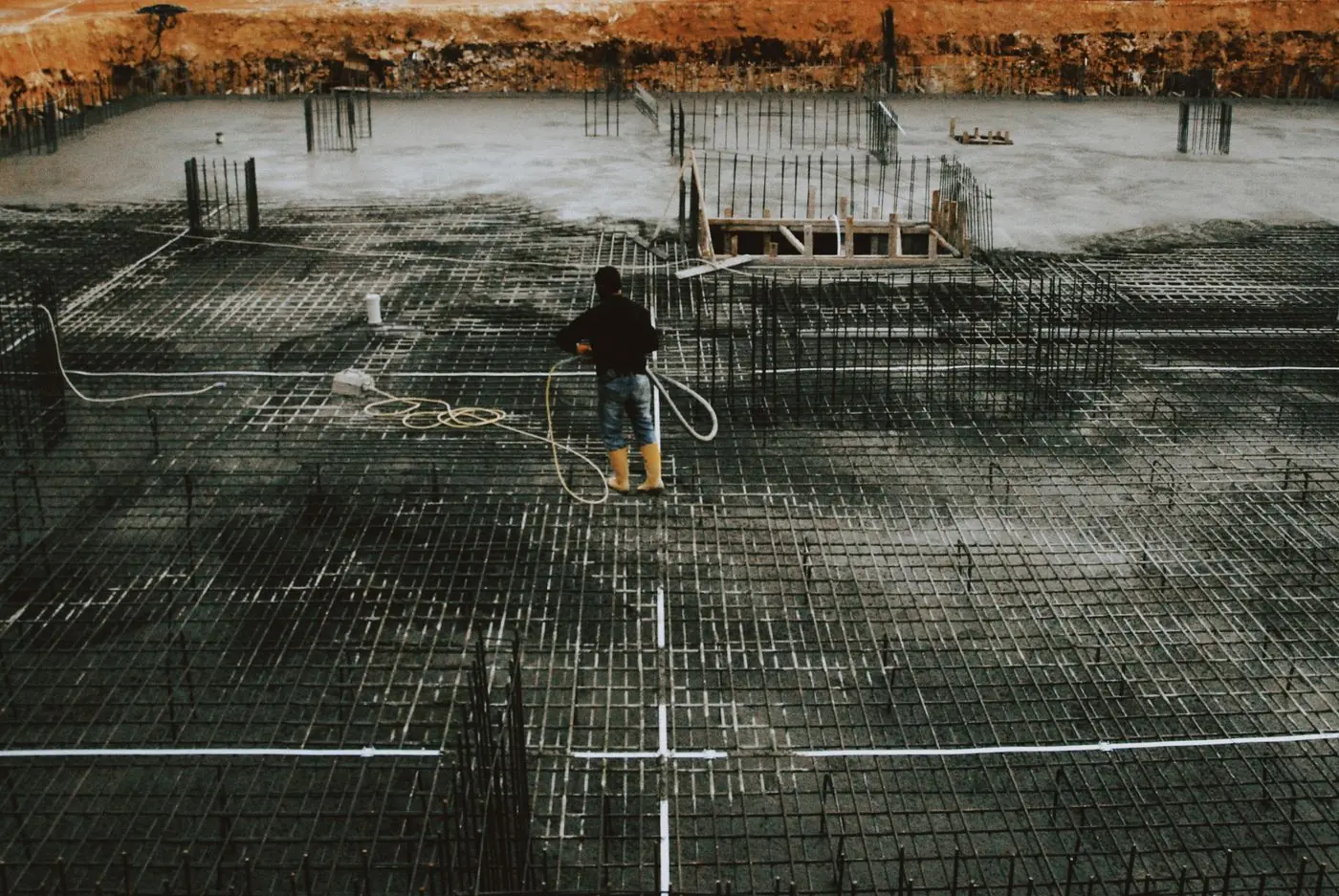 A reinforced concrete raft foundation on a construction site, steel reinforcement laid over a poured concrete base