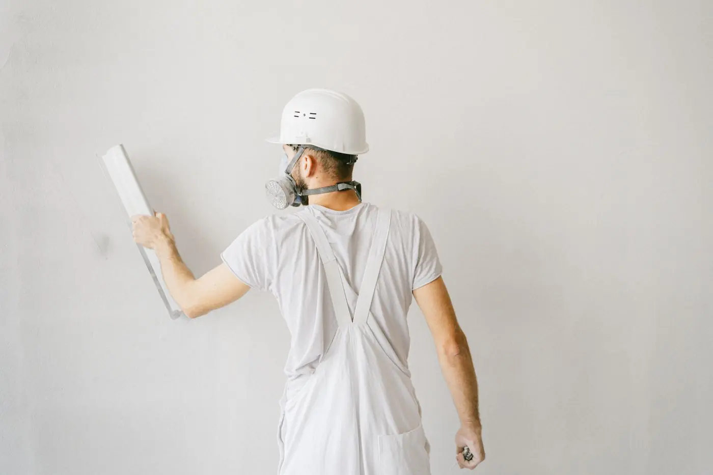 A plasterer in white overalls skimming an interior wall with a finishing trowel